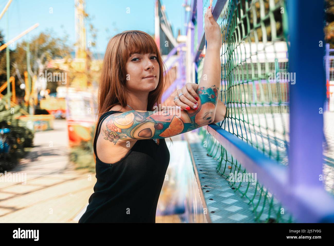 Portrait of a tanned young woman with tattoo sleeve posing near a fence. The concept of freedom and psychology. Stock Photo