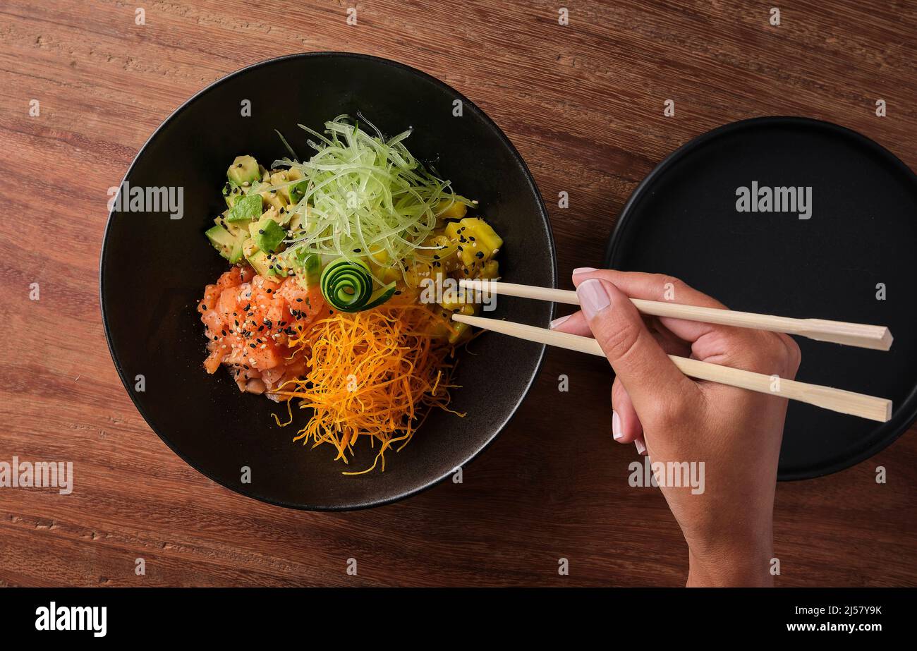 Woman eating traditional Hawaiian dish poke bowl with fork. Diet and Useful fast food. Selective focus. Stock Photo
