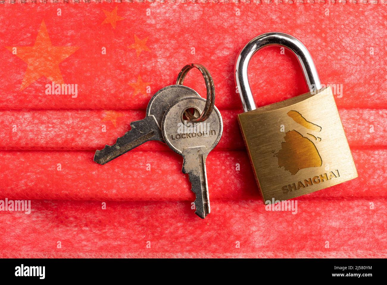 Shanghai lockdown: a lock with a Shanghai map and the word lockdown engraved on a pair of key over a surgical mask with chinese flag Stock Photo