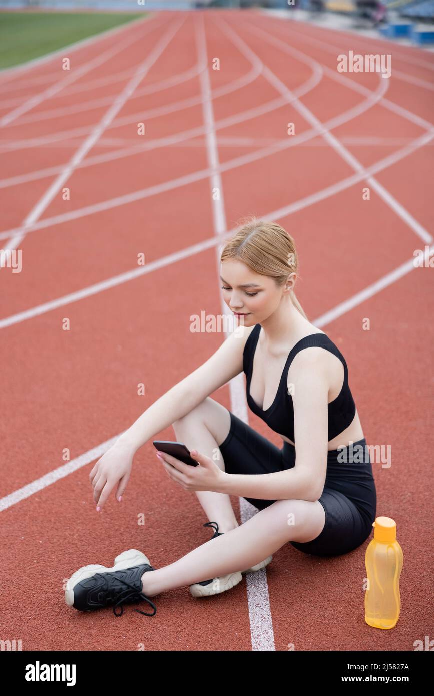 young sportive woman sitting with crossed legs and using cellphone Stock Photo