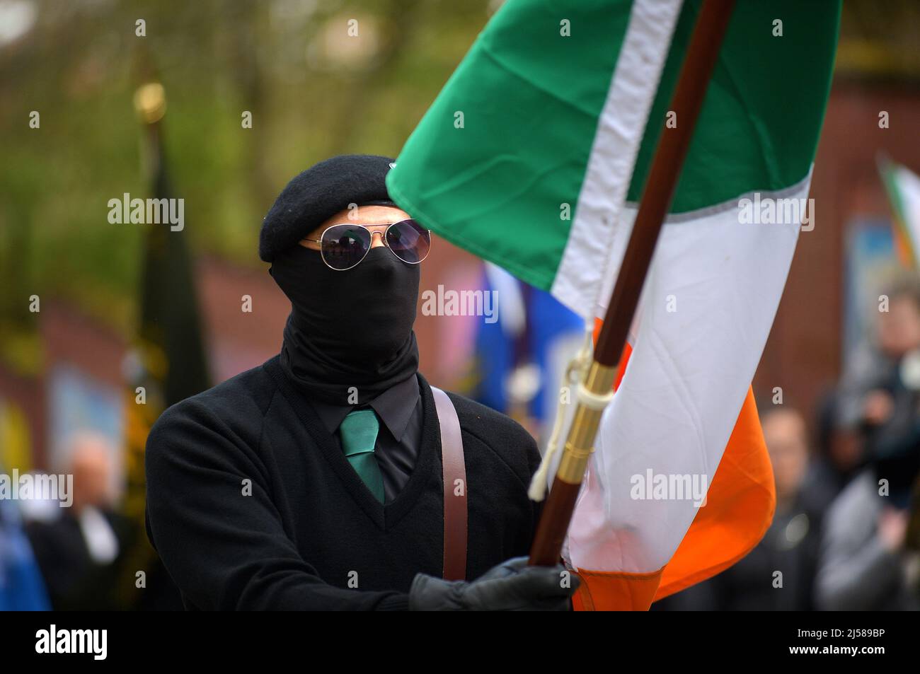 Masked men and women in paramilitary uniform at an Easter Masked man in paramilitary uniform carries Irish tricolour flag at an Easter Monday Dissident Republican parade in Derry, Northern Ireland 18 March 2022. ©George Sweeney / Alamy Stock Photo Stock Photo