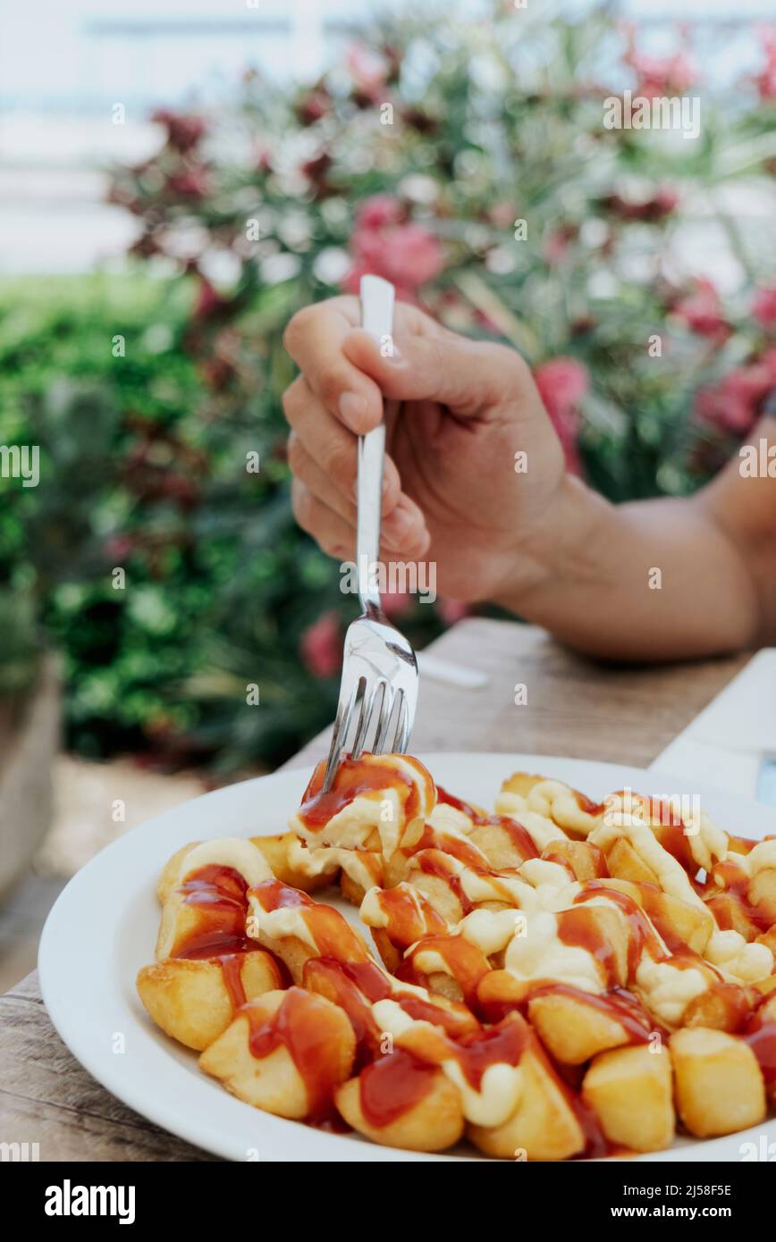 closeup of a man about to eat some typical spanish patatas bravas, fried potatoes with a hot sauce, sitting at an outdoors restaurant table Stock Photo