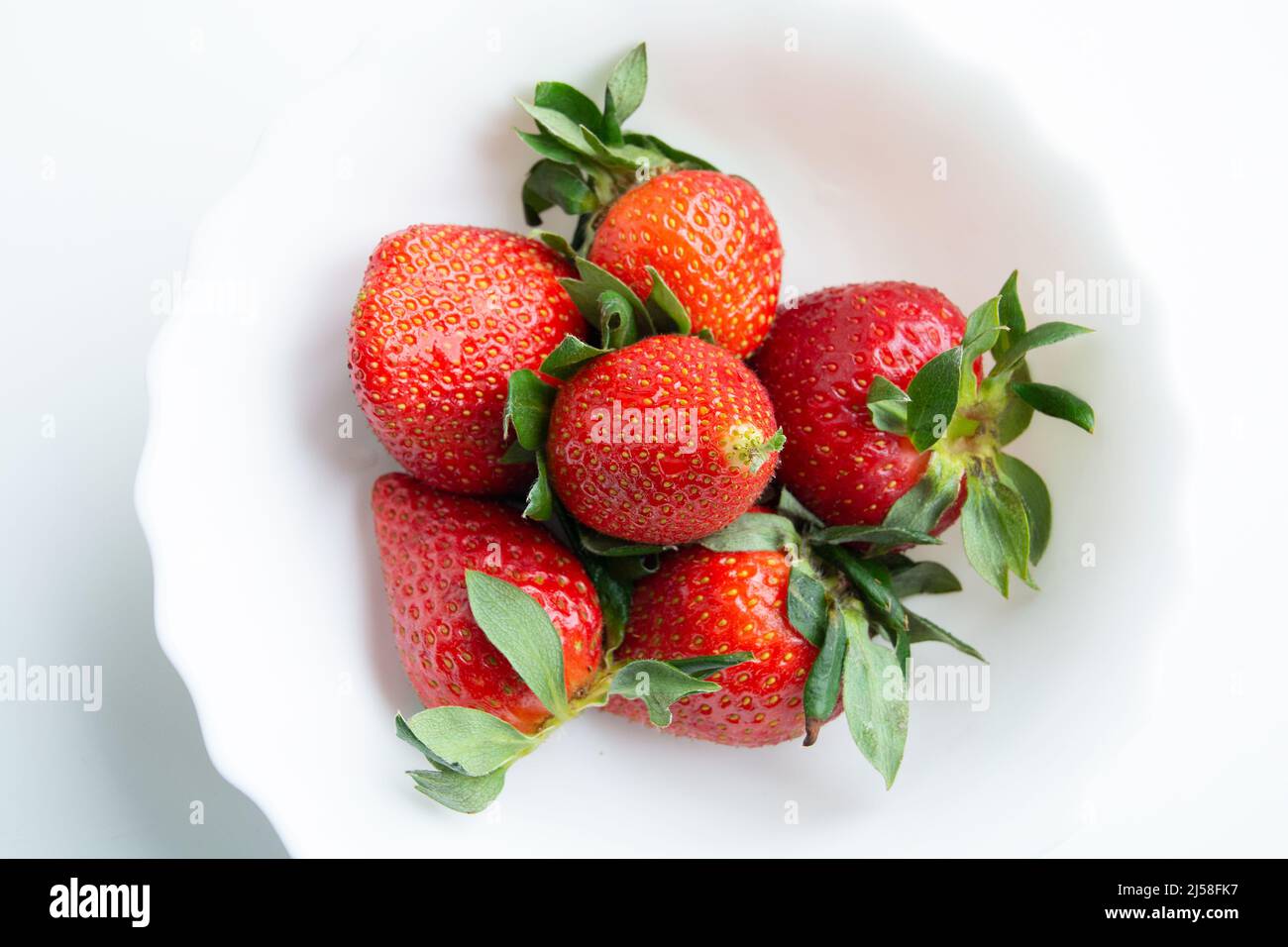 Strawberries in close-up composition. Some bright red berries on a white dish. Fruit seeds, between which one is already beginning to germinate. Stock Photo