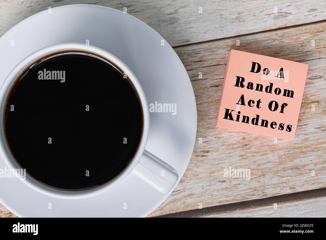 Motivational quote on notepad with white coffee cup on wooden desk - Do a random act of kindness. Stock Photo