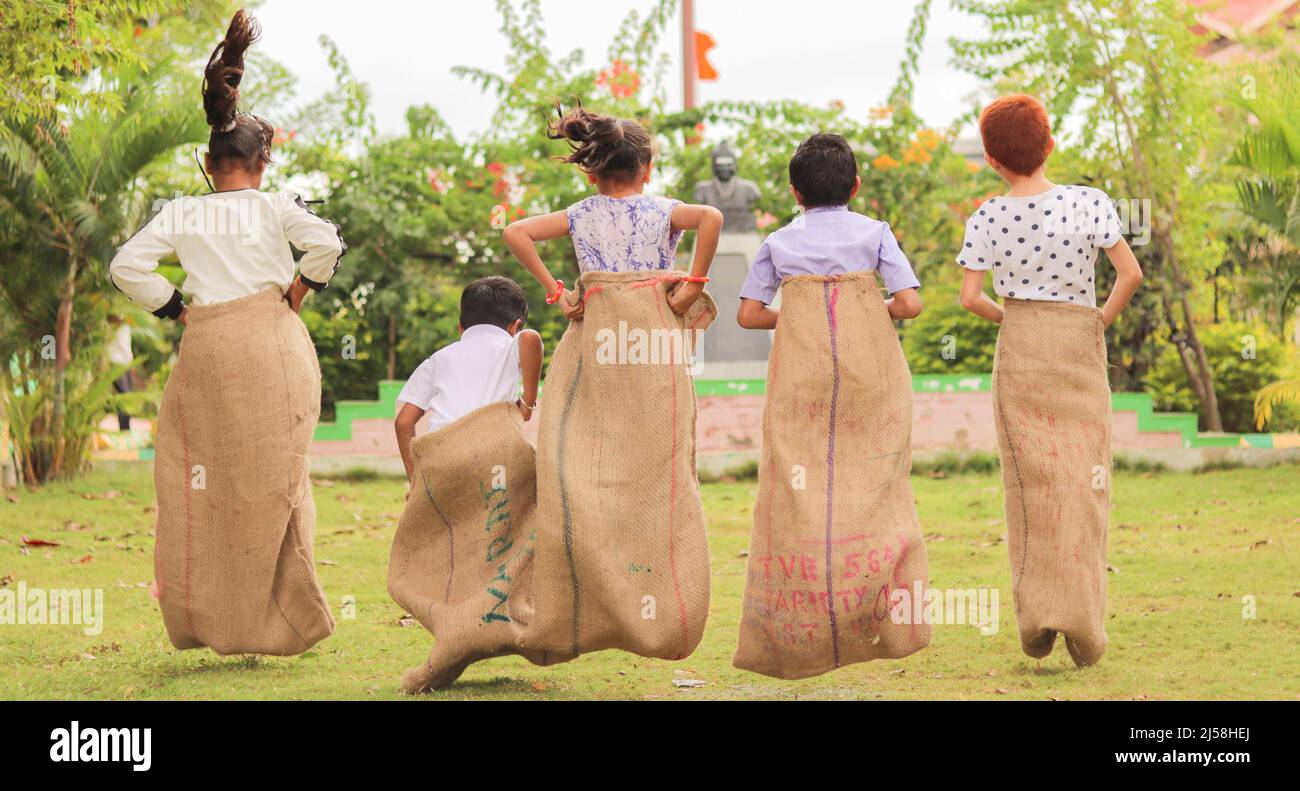back view shot of Group of Childrens playing potato sack jumping race game at park during summer camp - concept of childhood physical activities and Stock Photo