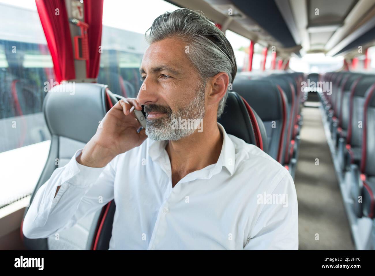 mature man talking on cellphone on empty bus Stock Photo