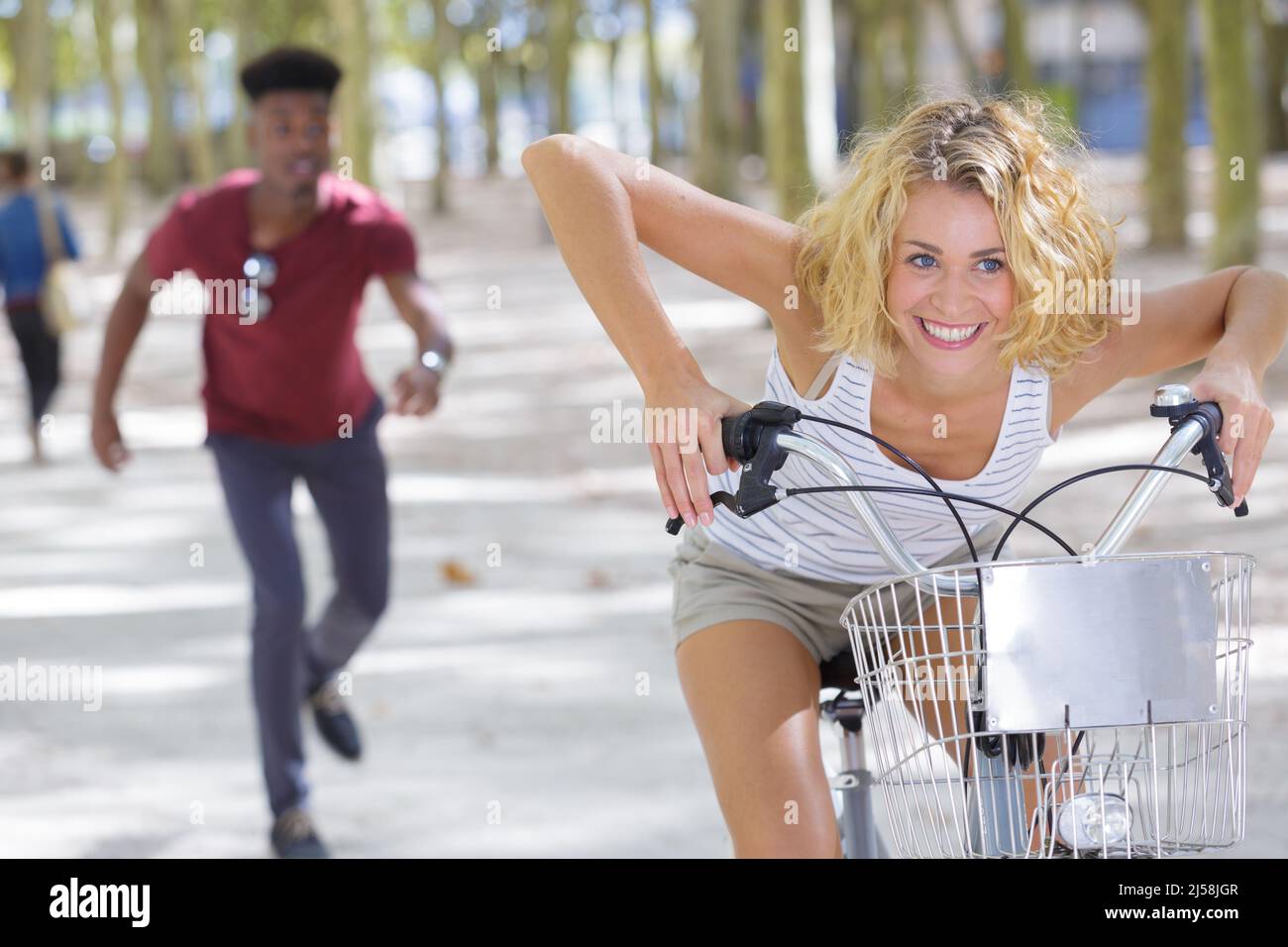 woman in bicycle racing male partner walking behind Stock Photo