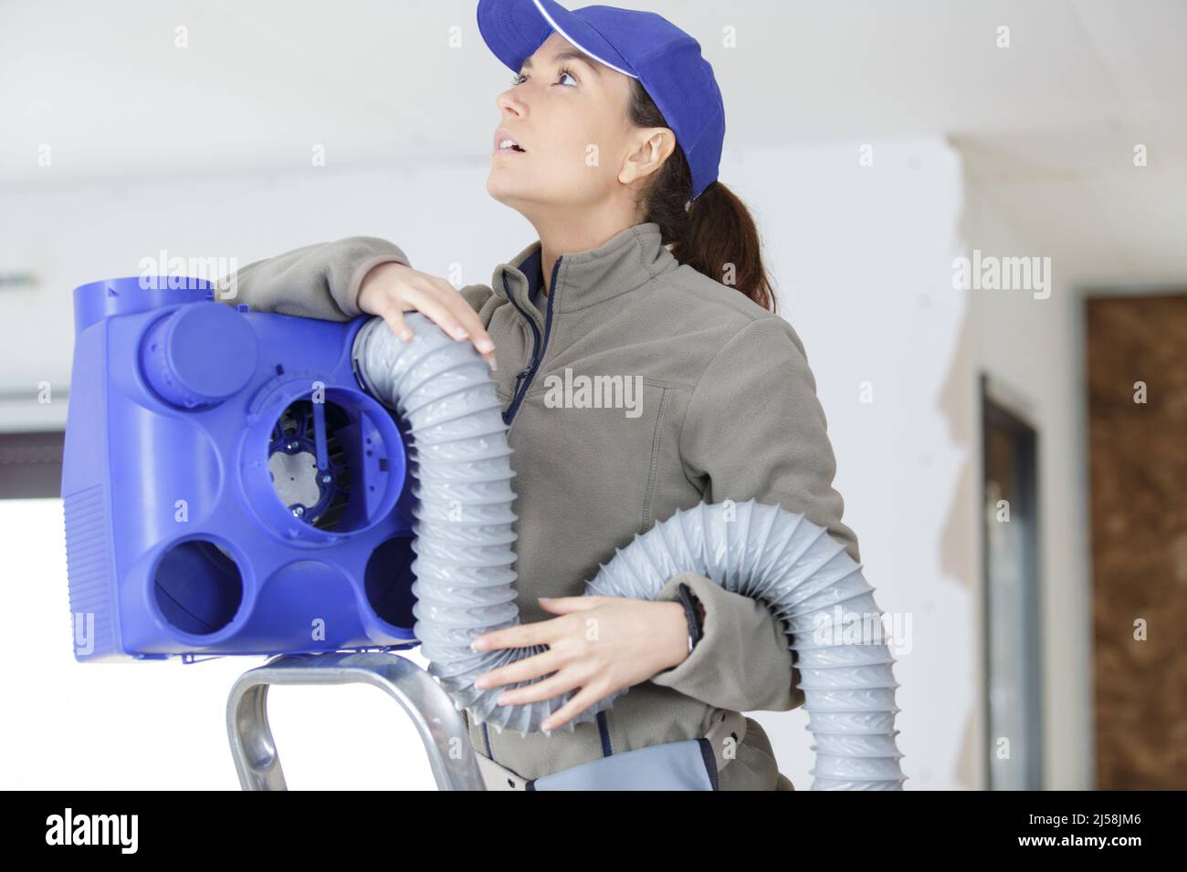female electrician fitting air conditions pipe in building ceiling Stock Photo