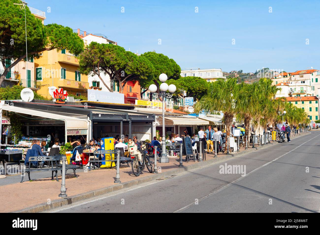 SANREMO, ITALY - OCTOBER 28, 2021: People sitting in sidewalk restaurant by road in bright sunlight Stock Photo