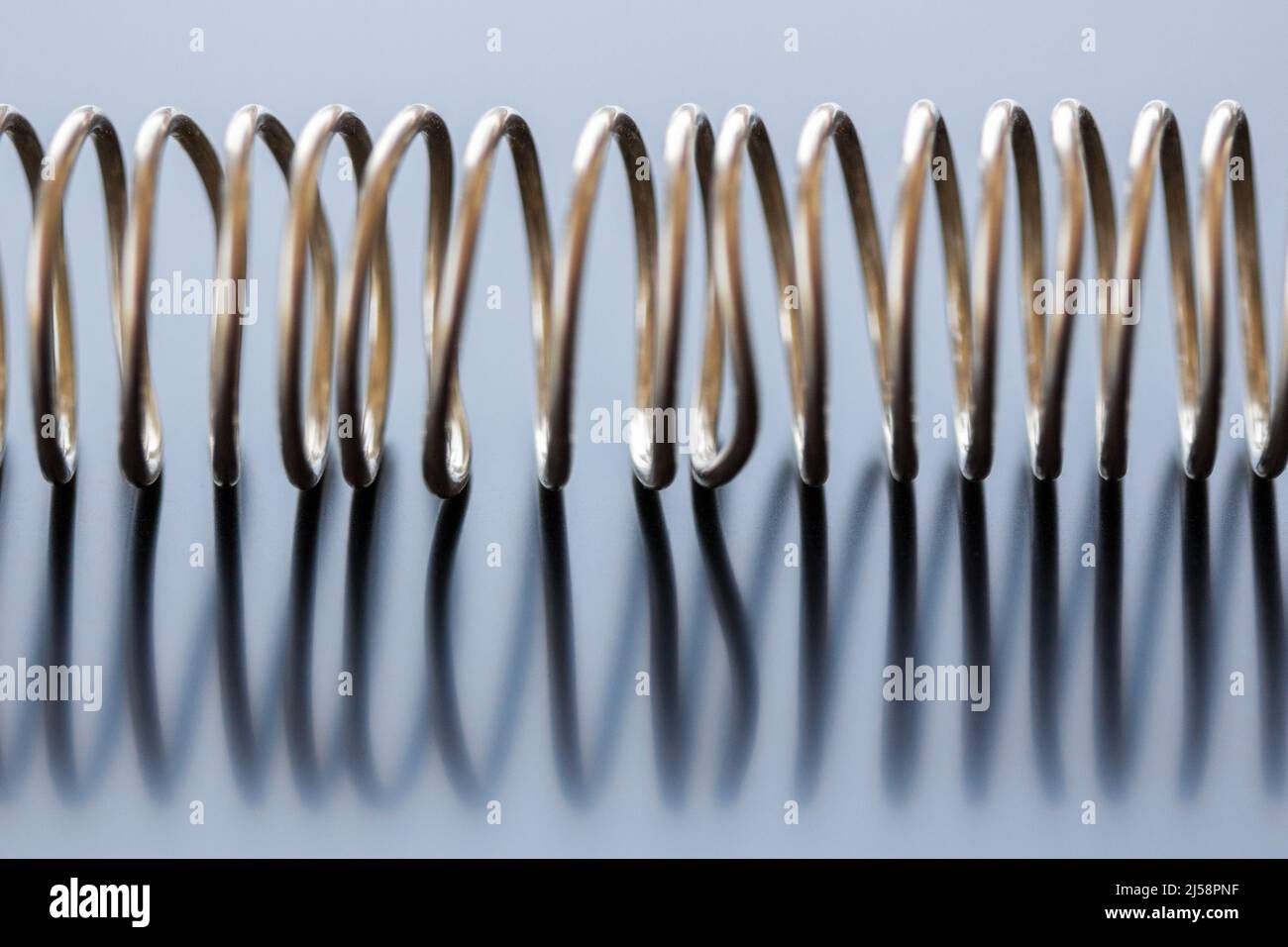 A coil of lead wire, shaped into a spiral, on a reflective surface makes an abstract design