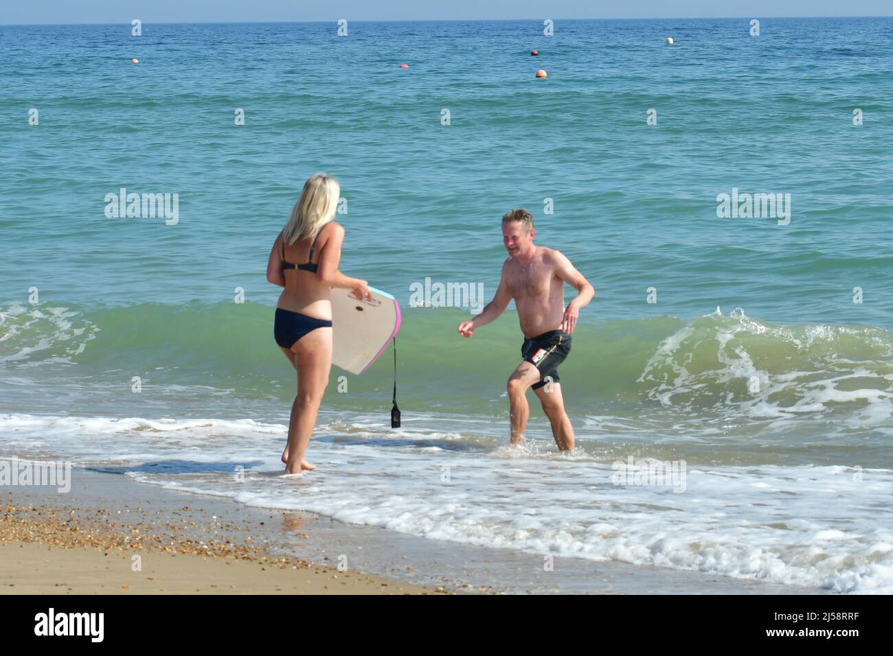 Boscombe, Bournemouth, Dorset, UK, 21st April 2022, Weather. Warm bright sunshine and above average temperatures in the afternoon brings people to the beach. Couple braving the cold sea with a bodyboard. Credit: Paul Biggins/Alamy Live News Stock Photo