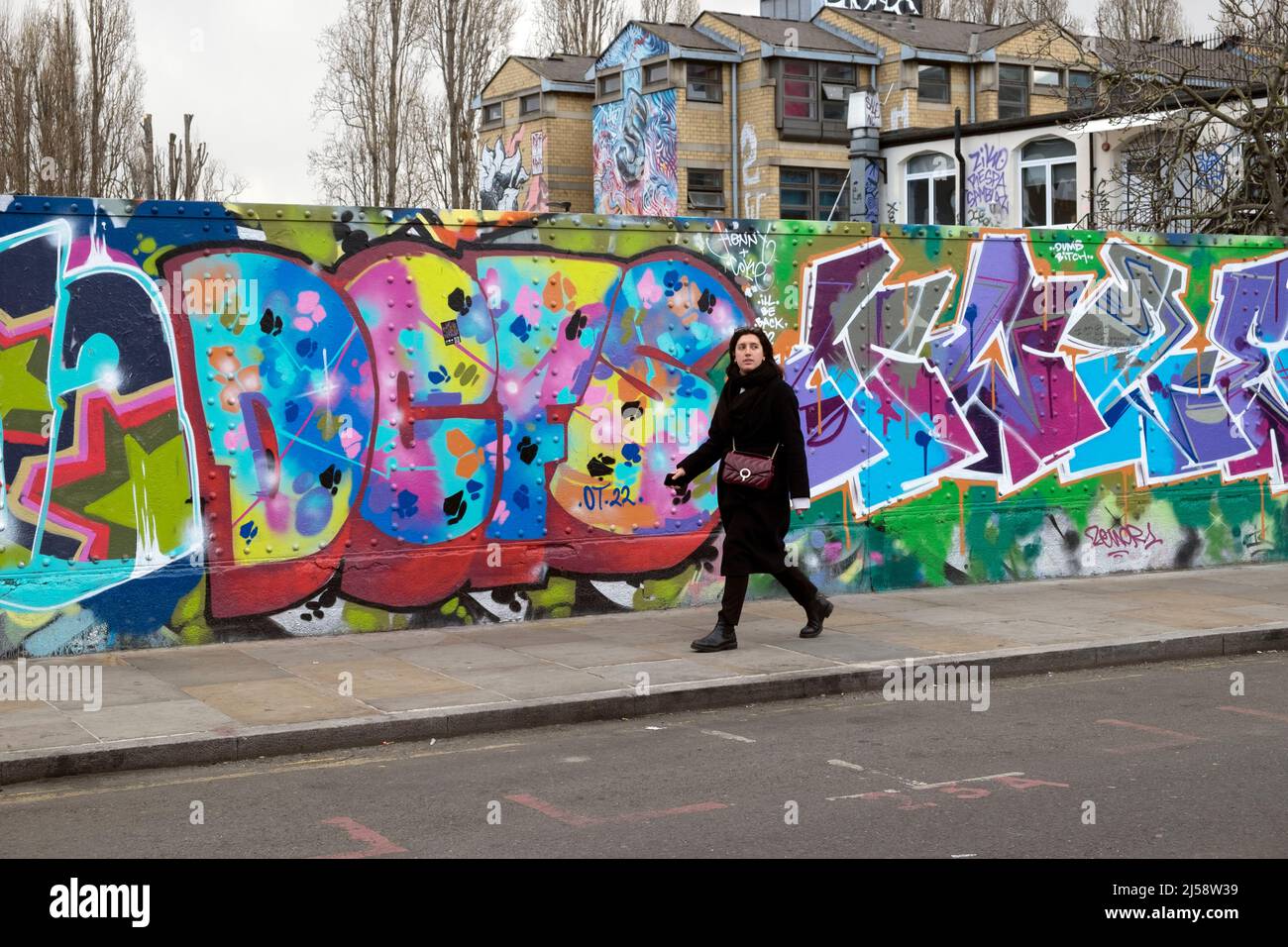 People person walking by colourful graffiti painting on hoardings in Brick Lane Shoreditch spring April 2022 London England UK  KATHY DEWITT Stock Photo