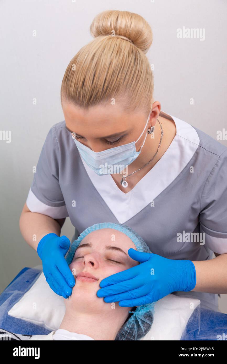 A female cosmetologist manually treats the patient's skin with a moisturizing and toning gel. The procedure helps to control the balance of fat conten Stock Photo