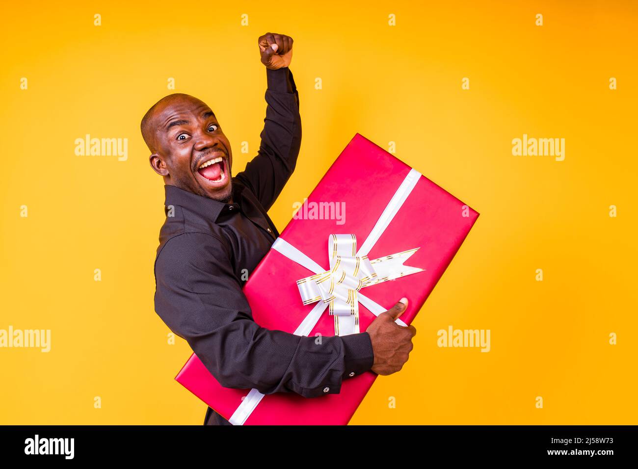 hispanic american man in black t-shirt getting big gift box in studio yellow background Stock Photo