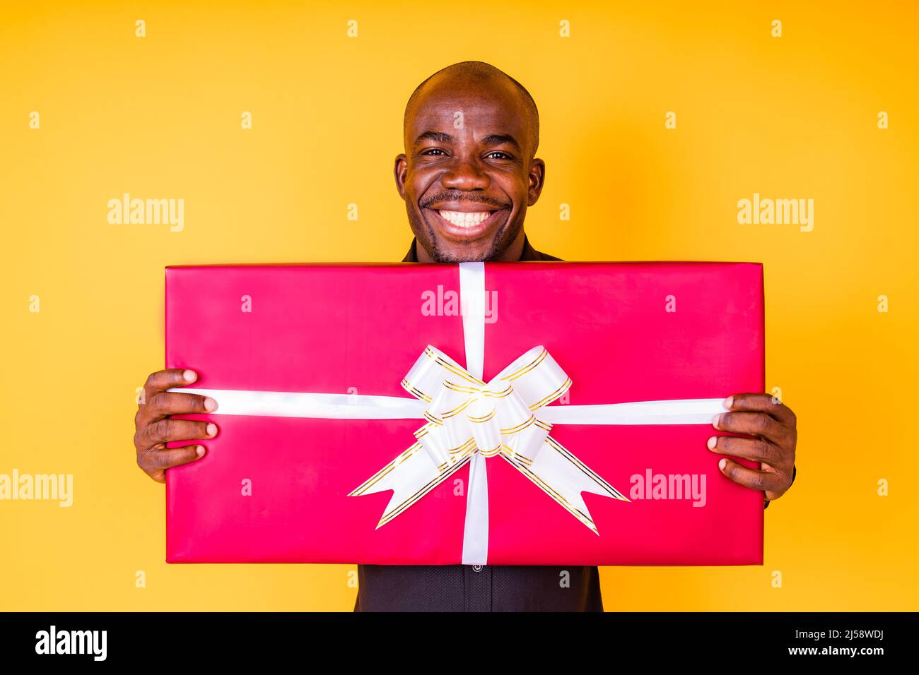 hispanic american man in black t-shirt getting big gift box in studio yellow background Stock Photo
