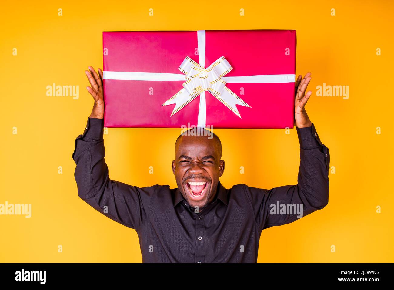 hispanic american man in black t-shirt getting big gift box in studio yellow background Stock Photo