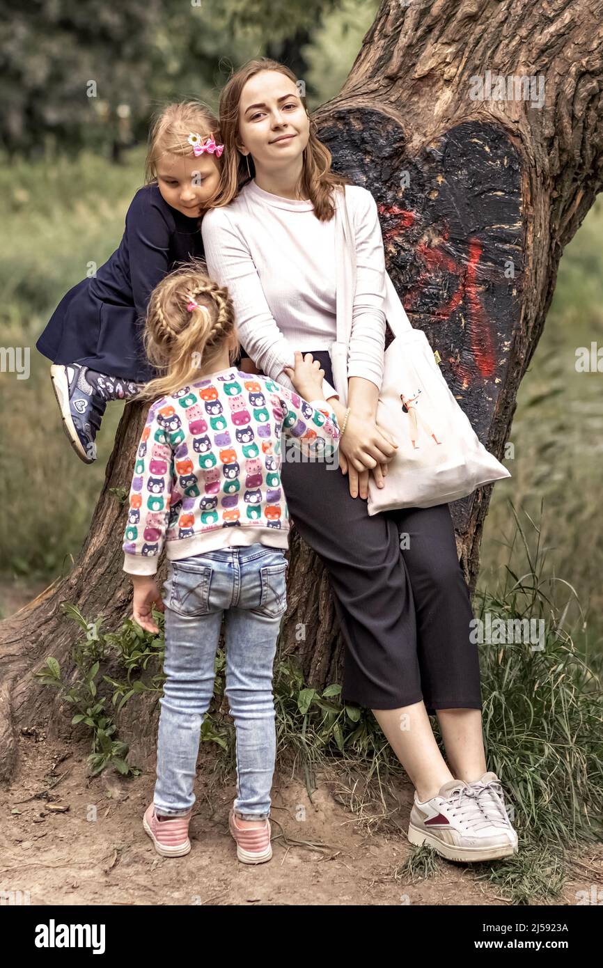 Three sisters at a tree in the spring park. A family walk Stock Photo