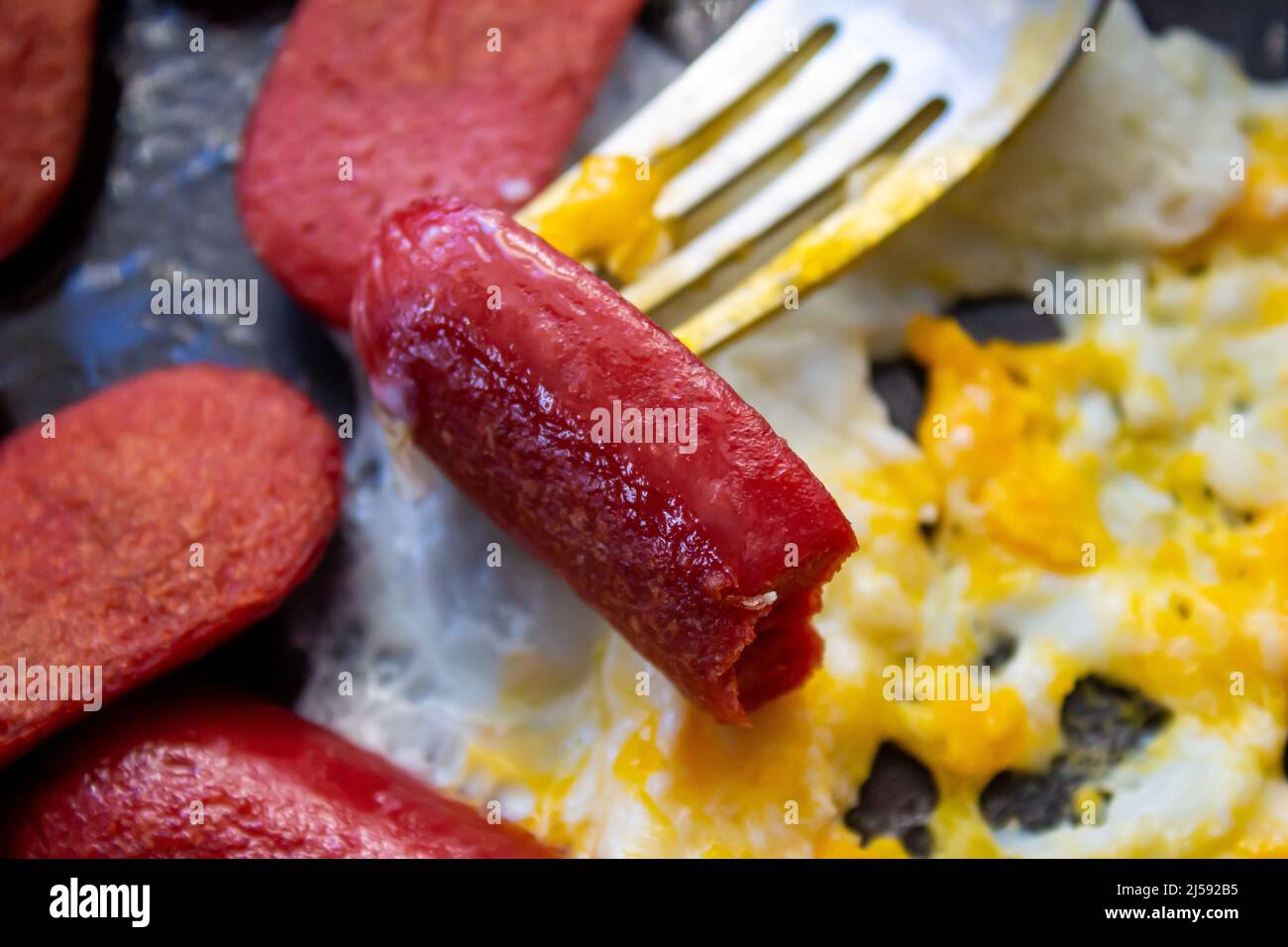 Fried egg with sausage. Unhealthy breakfast food. Closeup photo of eaten sausage. Stock Photo