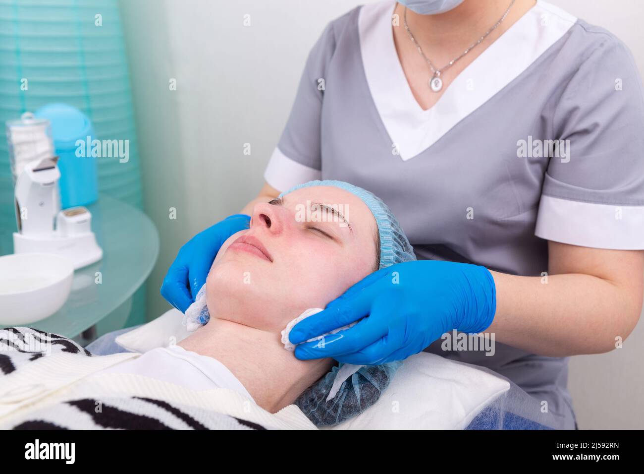 The cosmetologist treats the skin of the face with a tonic in order to moisturize and cleanse the skin before cosmetic procedures Stock Photo