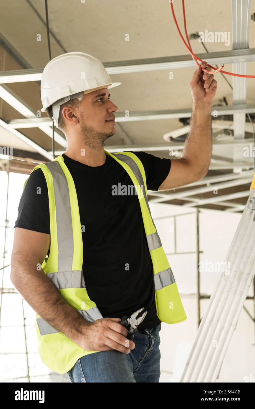 Young electrician cutting wires during his work on a construction site ...