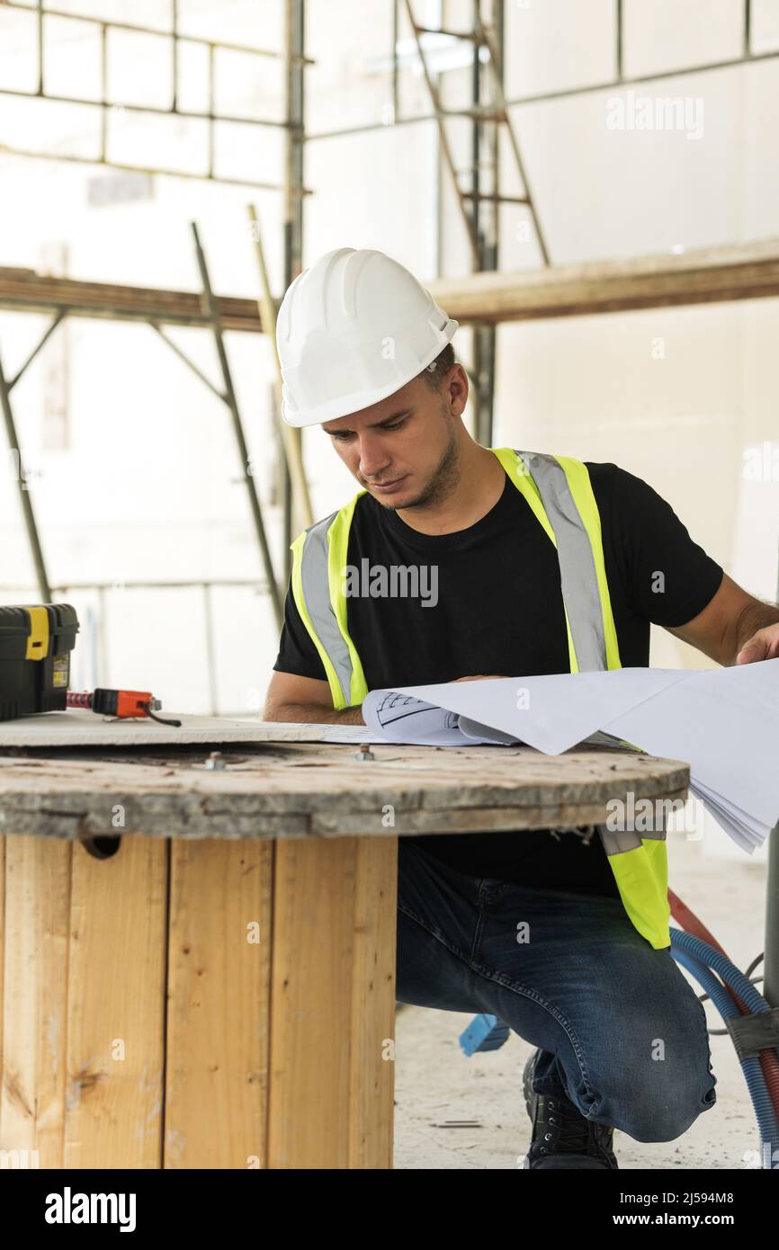 Young is worker checking blueprints during his work on a construction site Stock Photo