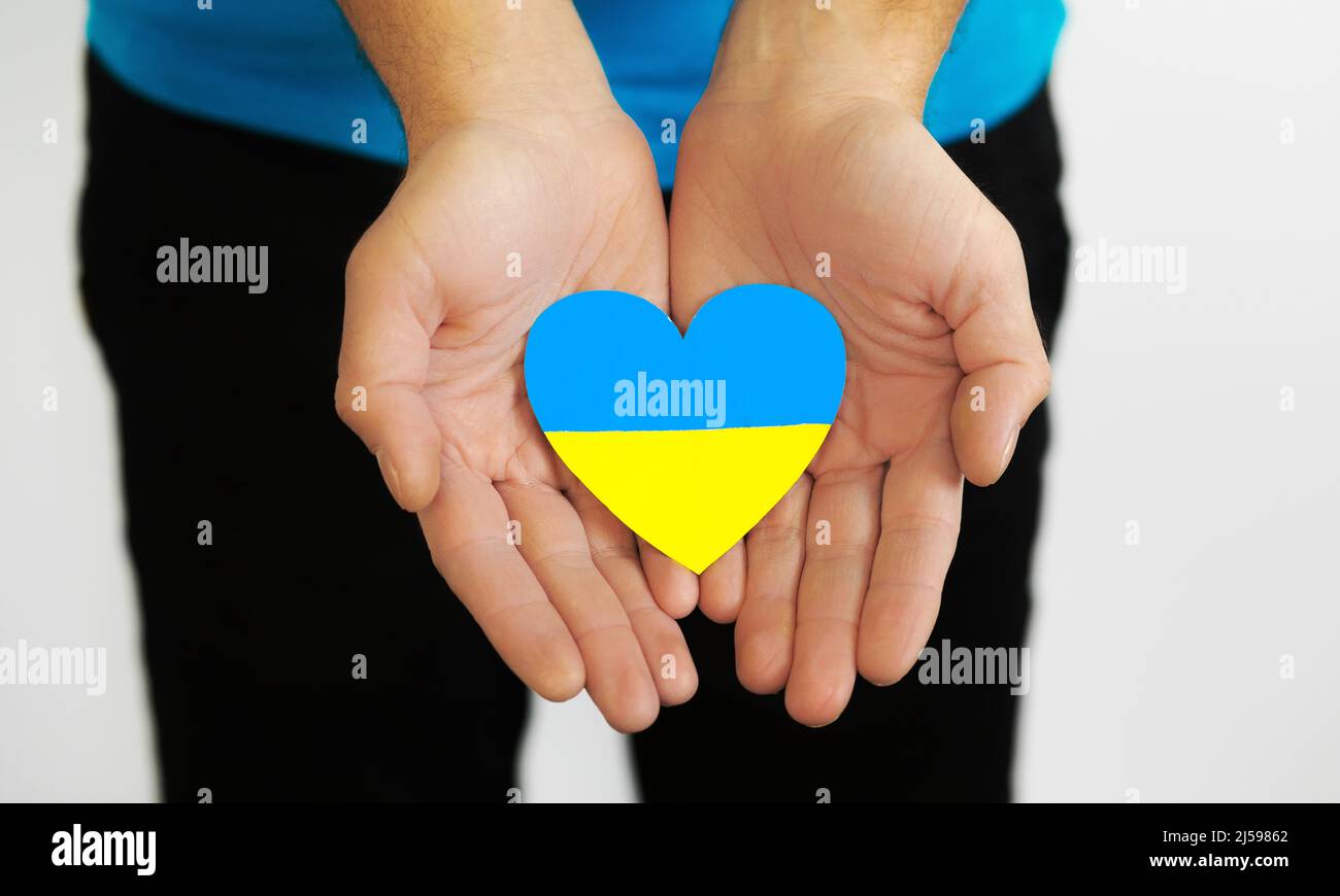 Love Ukraine concept. Ukrainian flag in the shape of a heart in the hands of a man. Ukrainian symbols, the flag of Ukraine - yellow and blue. Stock Photo