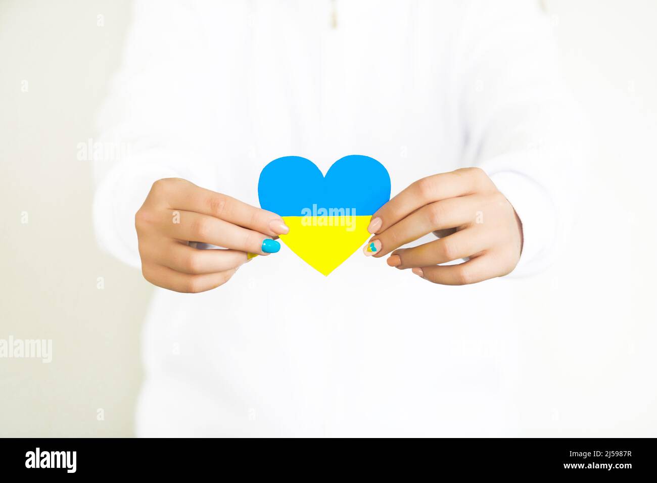 The concept of love for Ukraine. heart in the colors of the flag of Ukraine in female hands on a white background. Stock Photo