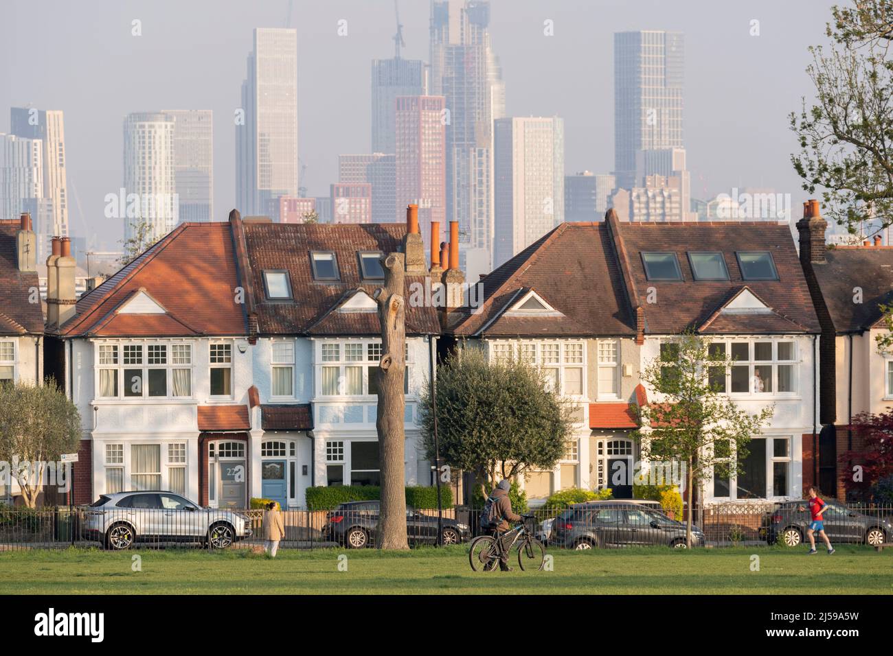 South Londoners walk in front of terraced period homes and in the distance, the growing development at Nine Elms at Battersea, seen from Ruskin Park, a south London green space in Lambeth, on 21st April 2022, in London, England. Stock Photo