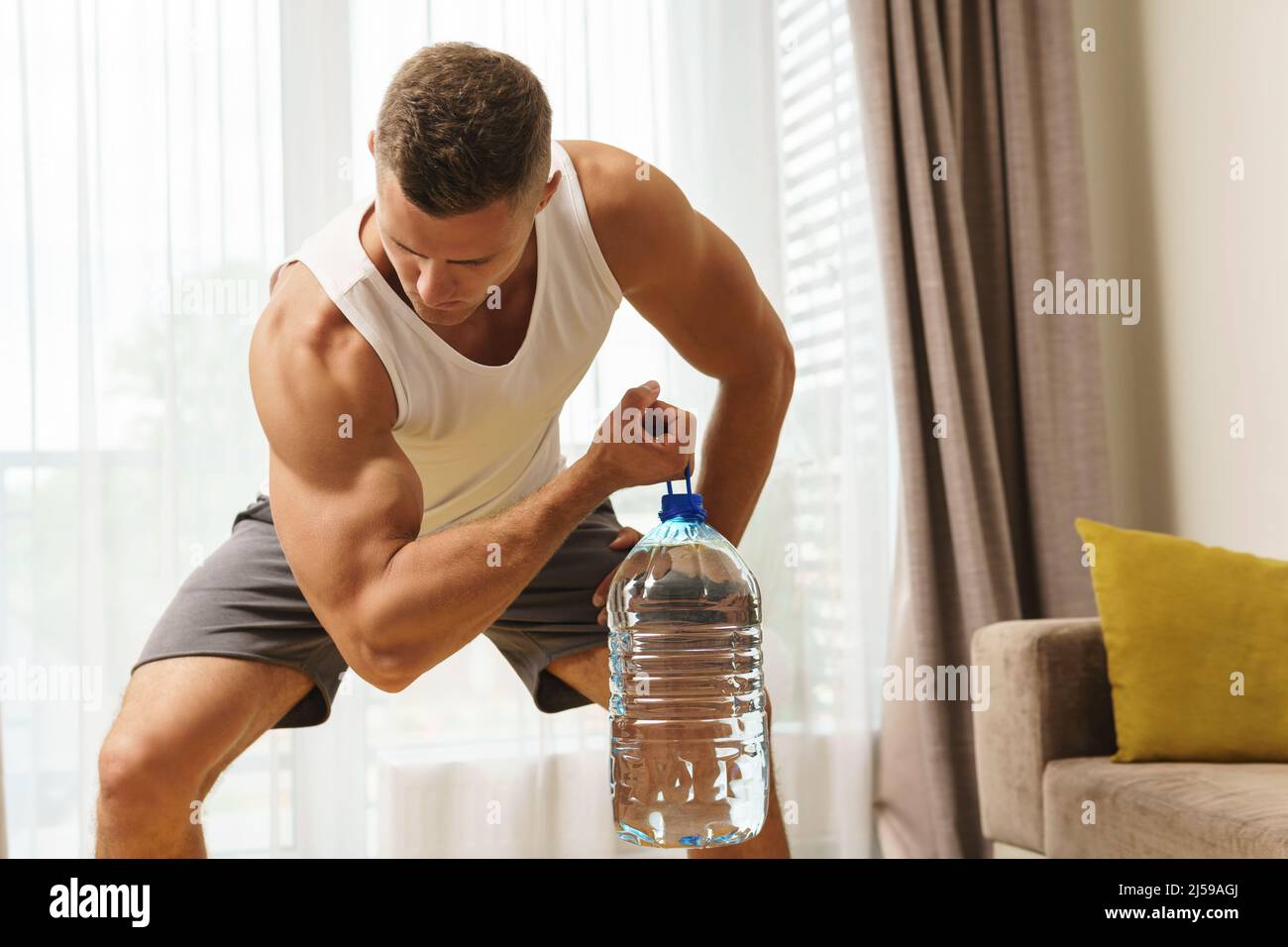 https://c8.alamy.com/comp/2J59AGJ/young-athletic-man-using-big-bottle-of-water-like-an-alternative-of-dumbbell-for-home-workout-2J59AGJ.jpg
