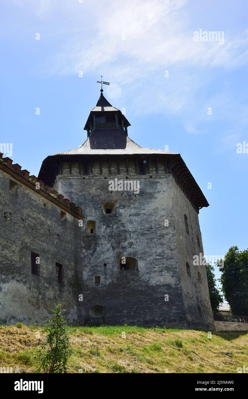 A powerful stone wall of a medieval fortress with many loopholes and embrasures. In the distance a large tower with a roof Stock Photo