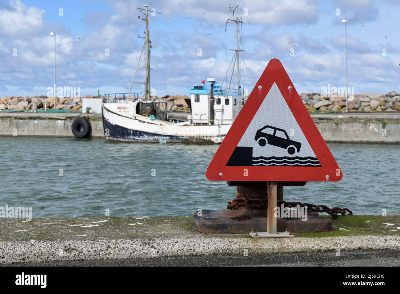 DENMARK, Jutland, Hirtshals, North Sea fishing port with fishing boat and traffic signboard Beware of dock you car may get drowned Stock Photo