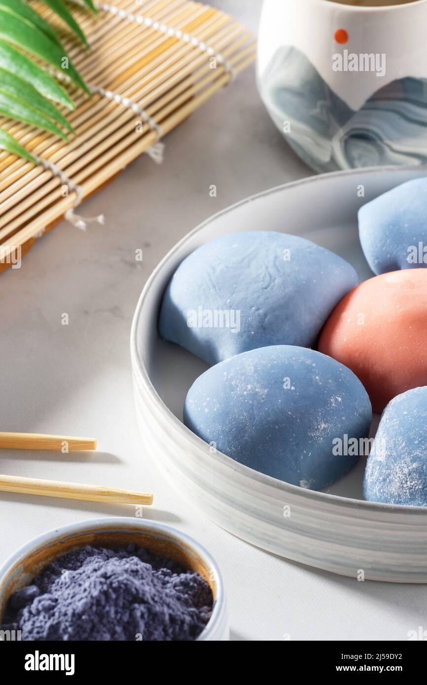 Concept of a traditional Japanese dessert. A ceramic bowl of Japanese mochi with chopsticks and maki sudare mat on white countertop. Asian rice cake Stock Photo