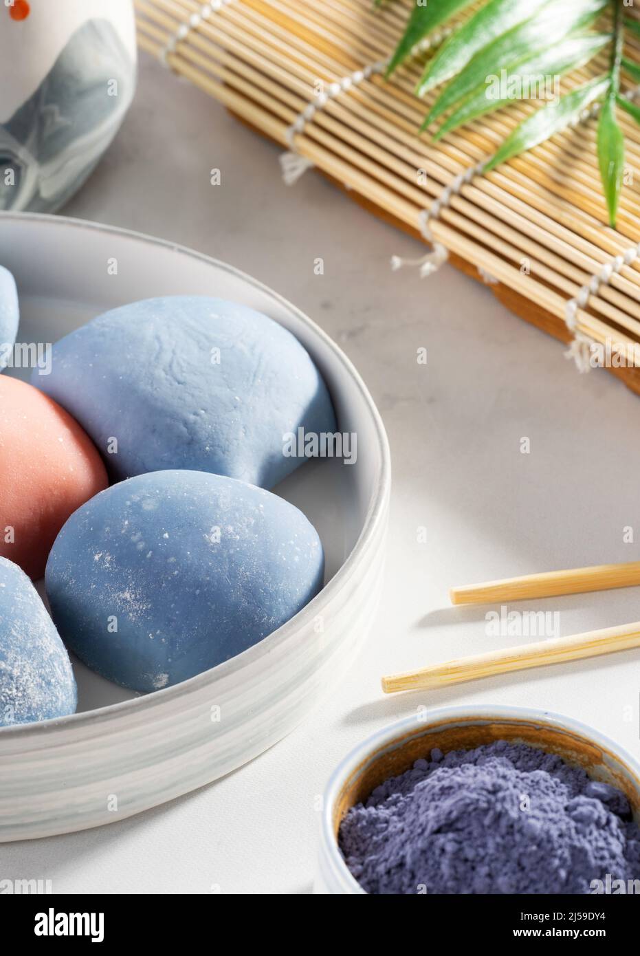 A bowl of Japanese mochi with chopsticks and wooden mat on white countertop. Concept of a traditional Japanese dessert on the kitchen table. Stock Photo