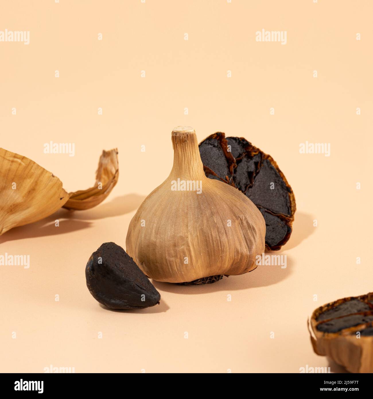 Black garlic bulbs, cloves and peel lie on a beige table. A conceptual