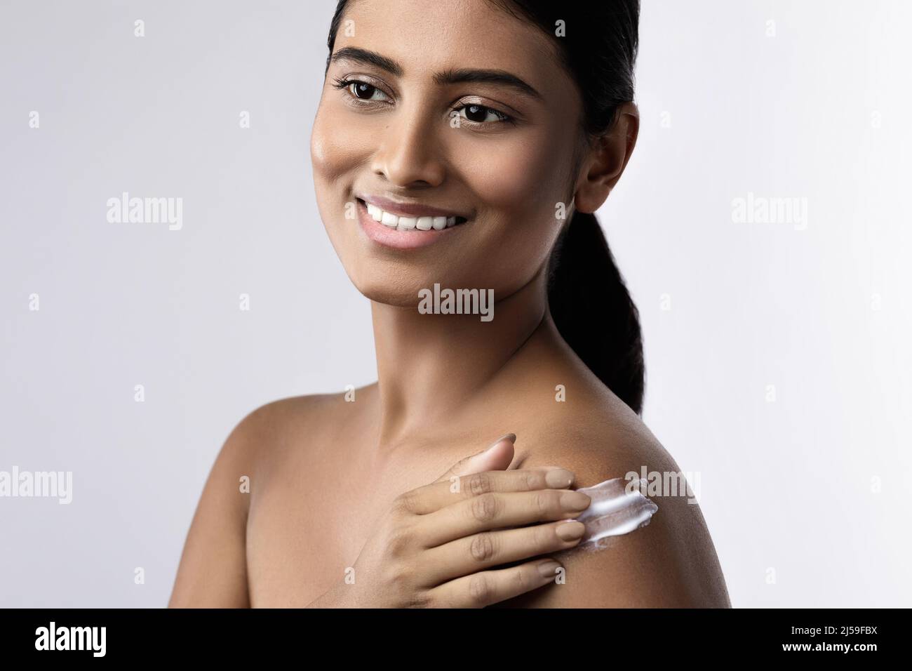 Beautiful and happy Indian woman applying moisturizing cream or sunblock lotion on her body Stock Photo
