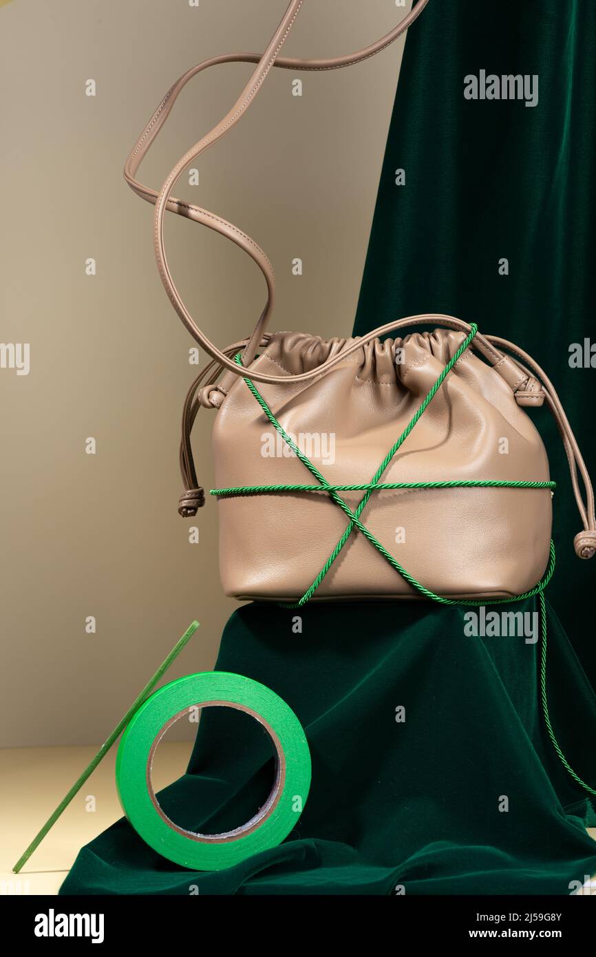 Coffee-colored handbag made from an artificial leather on a podium covered with green velvet on a beige background. Composition of faux leather bag Stock Photo