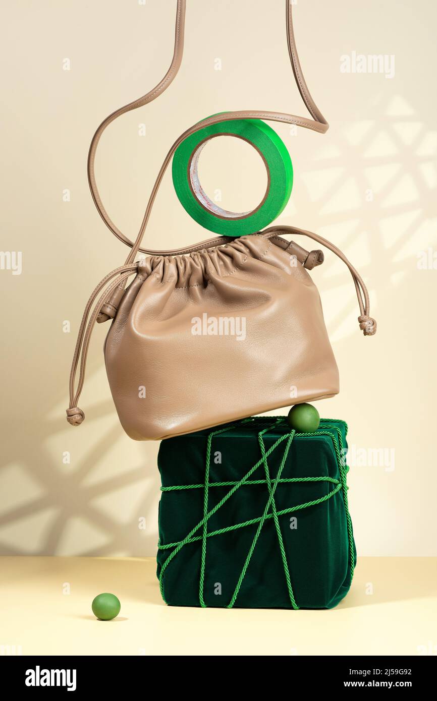 Conceptual creative modern Still life, balance composition. Beige handbag on a podium covered with green velvet. Eco-leather bag, velvet, tied Stock Photo