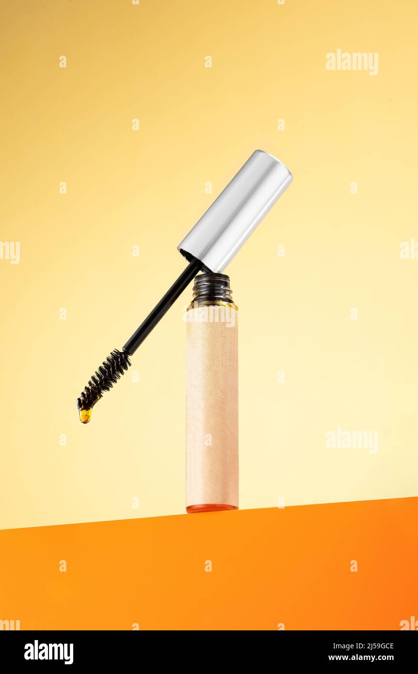 Castor oil for eyelashes and eyebrows in a vial with a brush on an orange background. Beauty concept, eyelash and eyebrow care, wellness, growth Stock Photo