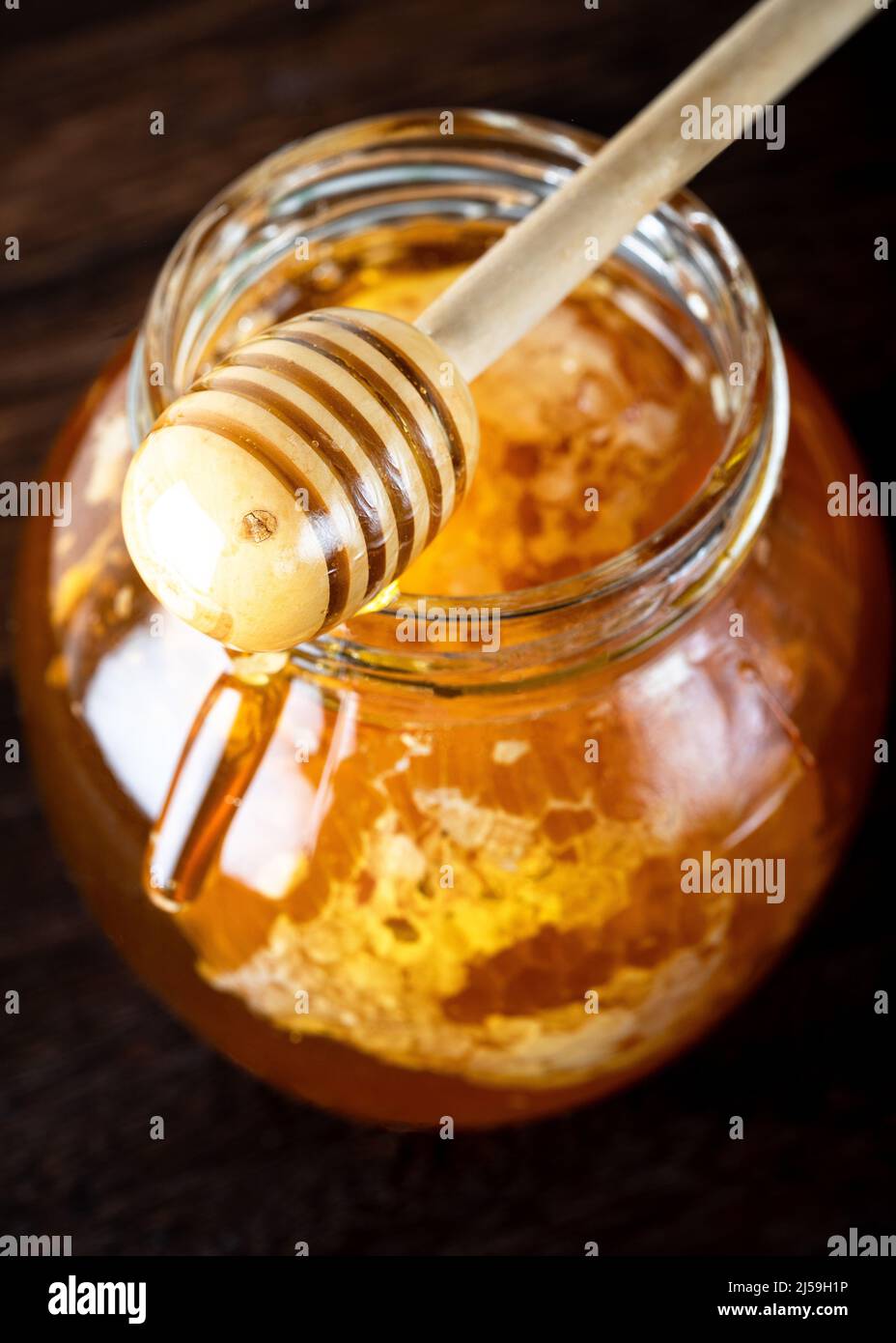Honey dipper pouring honey in the jar. Wooden honey dipper taking honey from the jar Stock Photo