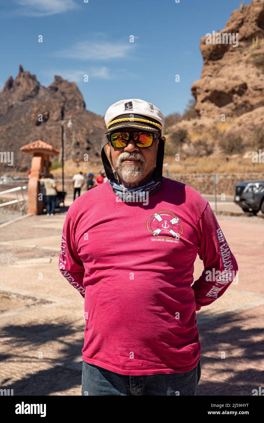 A charter boat captain in a red shirt stands on shore with his hands behind his back, Mount Tetakawi in the background, San Carlos, Sonora, Mexico. Stock Photo