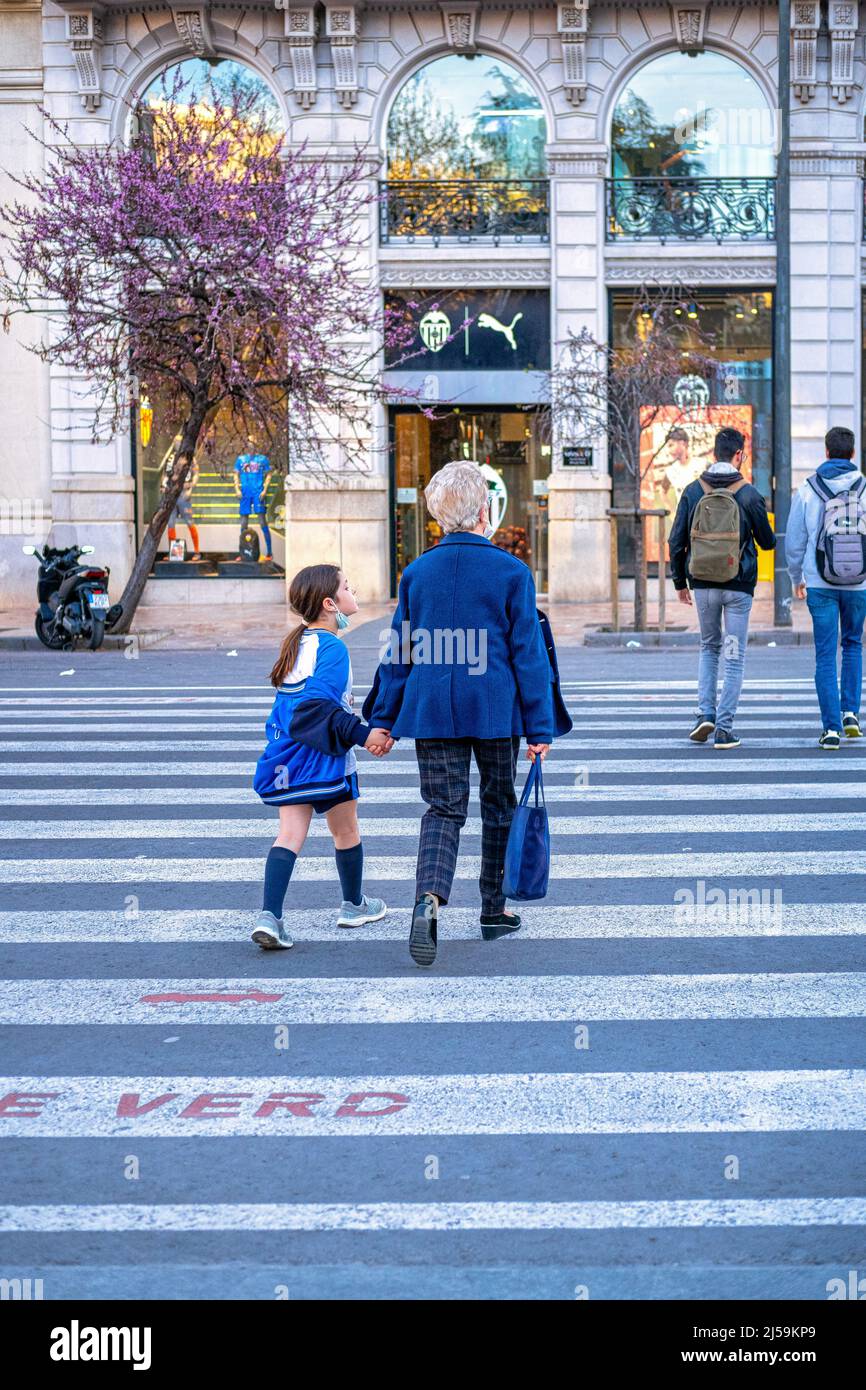 A senior woman and a female child cross the street using a crosswalk in the old town. This residential district is a famous place and a tourist attrac Stock Photo