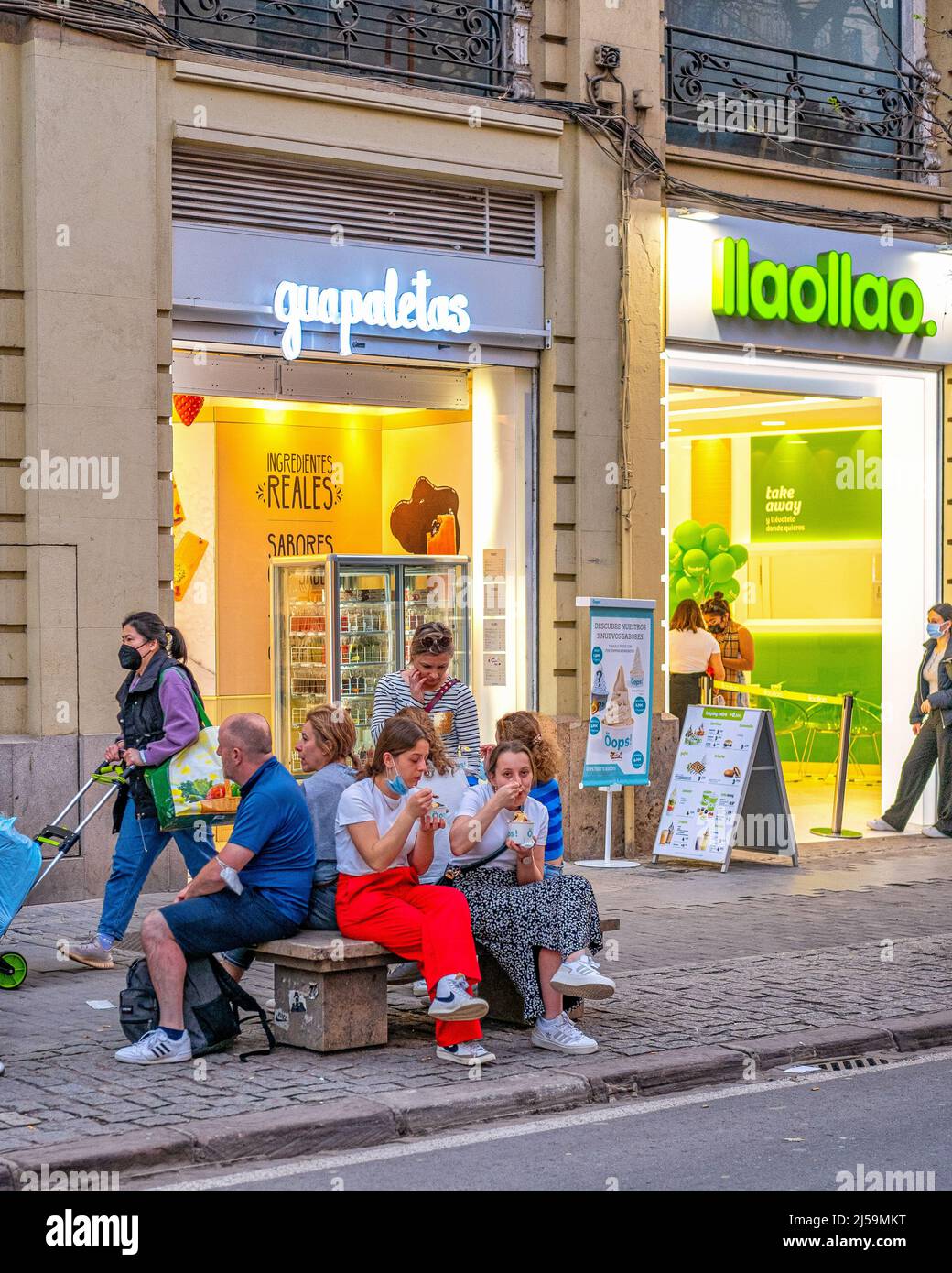 Tourists or people eating ice cream in a sidewalk bench by the small business named 'Guapaletas'.  The famous place is located in the old town. Stock Photo