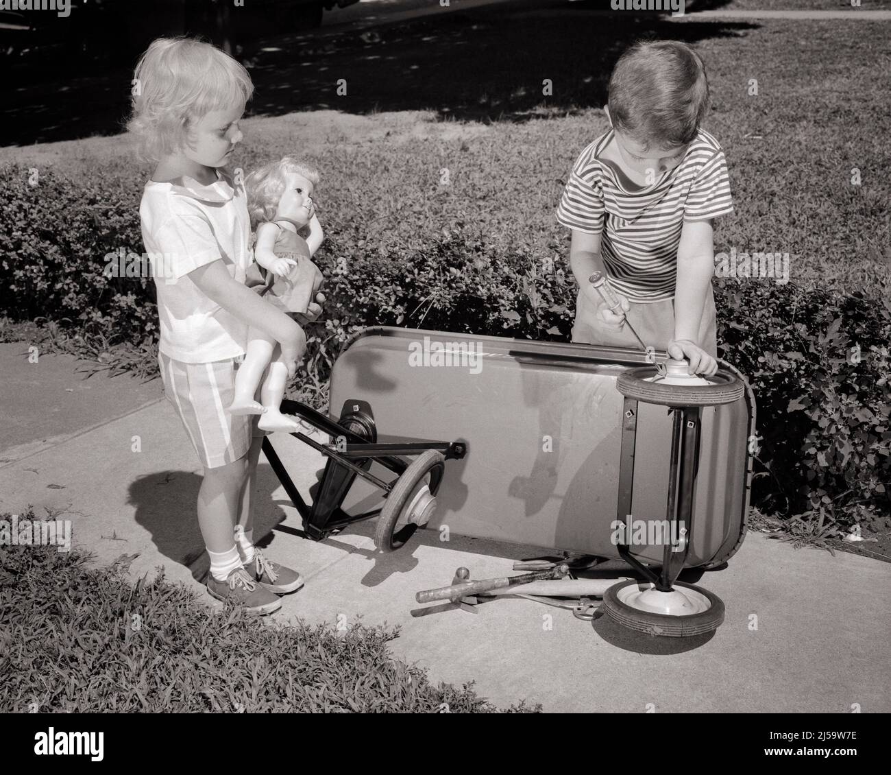 1960s BOY BROTHER FIXING REPAIRING TIRE WHEEL ON KID’S WAGON WHILE LITTLE GIRL SISTER CLUTCHING A DOLL WATCHES AND WAITS - j11116 HAR001 HARS TIRE HOME LIFE COPY SPACE FRIENDSHIP FULL-LENGTH PERSONS INSPIRATION CARING MALES SIBLINGS CONFIDENCE FIXING SISTERS TRANSPORTATION B&W GOALS SUCCESS HAPPINESS WATCHES AND KNOWLEDGE PROGRESS RECREATION PRIDE SIBLING REPAIRING CONNECTION CONCEPTUAL FAVOR FRIENDLY KID'S WAITS JUVENILES SOLUTIONS TOGETHERNESS BLACK AND WHITE CAUCASIAN ETHNICITY CLUTCHING HAR001 OLD FASHIONED Stock Photo