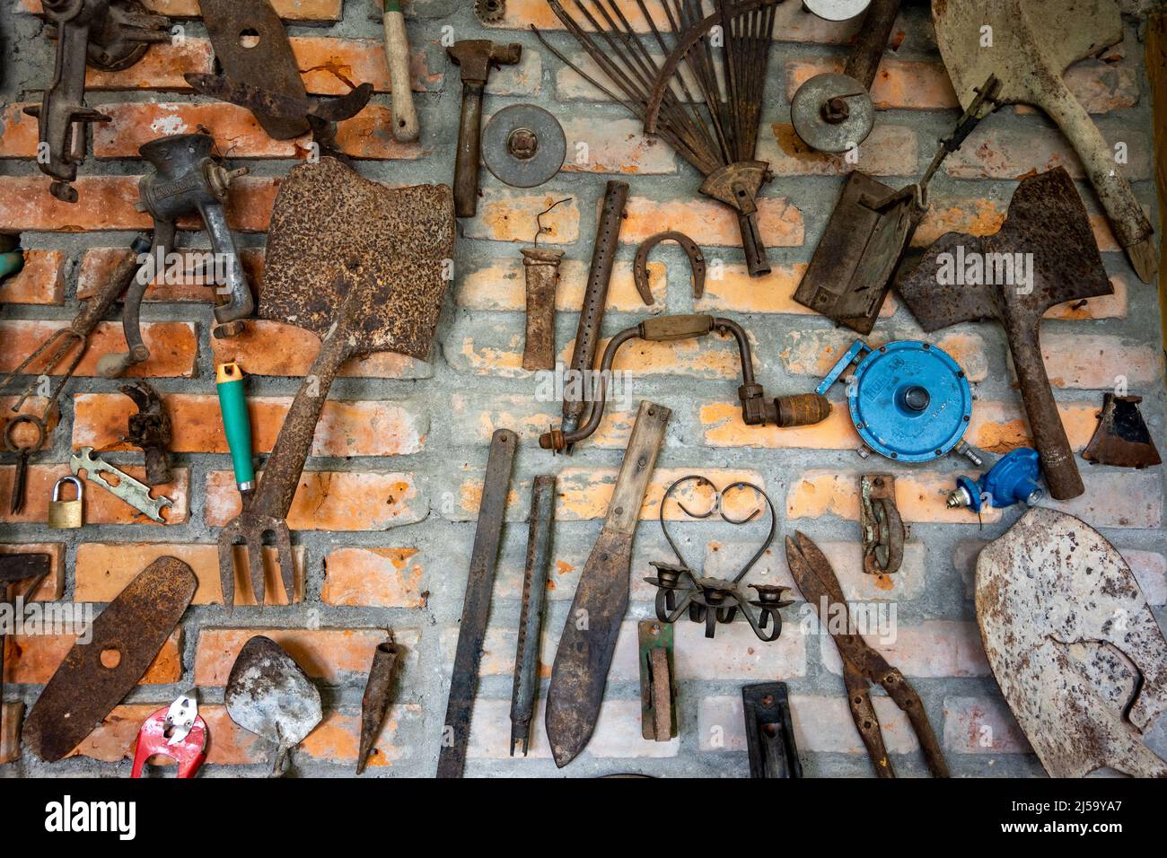 A collection of rusty hand tools mounted on a brick wall. Colombia, South America. Stock Photo
