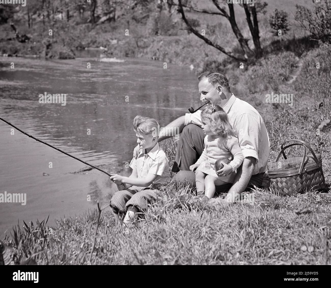 1930s FAMILY FISHING FATHER SITTING BY STREAM HIS SON HAS FISHING POLE IN WATER DAUGHTER SITTING ON HIS LAP BESIDE PICNIC BASKET - j2596 HAR001 HARS 3 DAD MEAL SMOKE NOSTALGIC PAIR BEAUTY SUBURBAN OLD TIME RIVER NOSTALGIA BROTHER OLD FASHION SISTER 1 JUVENILE POLE SECURITY YOUNG ADULT SAFETY POND TEAMWORK SONS PLEASED FAMILIES JOY LIFESTYLE FEMALES BROTHERS PIPE RURAL HEALTHINESS HOME LIFE COPY SPACE FULL-LENGTH HALF-LENGTH DAUGHTERS PERSONS INSPIRATION STREAM CARING MALES HOOK SERENITY SIBLINGS CONFIDENCE SISTERS FATHERS B&W LAP CATCHING SUCCESS HAPPINESS WELLNESS CHEERFUL ADVENTURE HIS Stock Photo