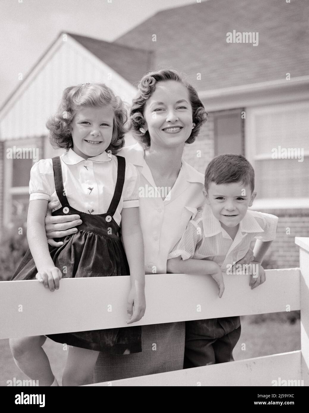 1950s PORTRAIT SMILING MOTHER AND TWO CHILDREN BOY AND GIRL LEANING ON WHITE FENCE IN FRONT OF SUBURBAN HOUSE LOOKING AT CAMERA - j6119 HAR001 HARS MOTHERS OLD TIME NOSTALGIA LEANING MEDIA OLD FASHION SISTER 1 JUVENILE SONS PLEASED FAMILIES JOY SATISFACTION FEMALES HOUSES HEALTHINESS HOME LIFE FRIENDSHIP HALF-LENGTH LADIES DAUGHTERS PERSONS RESIDENTIAL CUTOUT MALES BUILDINGS CONFIDENCE SISTERS B&W EYE CONTACT HAPPINESS CHEERFUL AND PRIDE HOMES SMILES CONNECTION JOYFUL RESIDENCE COOPERATION GROWTH MID-ADULT MOMS TOGETHERNESS BLACK AND WHITE HAR001 OLD FASHIONED Stock Photo