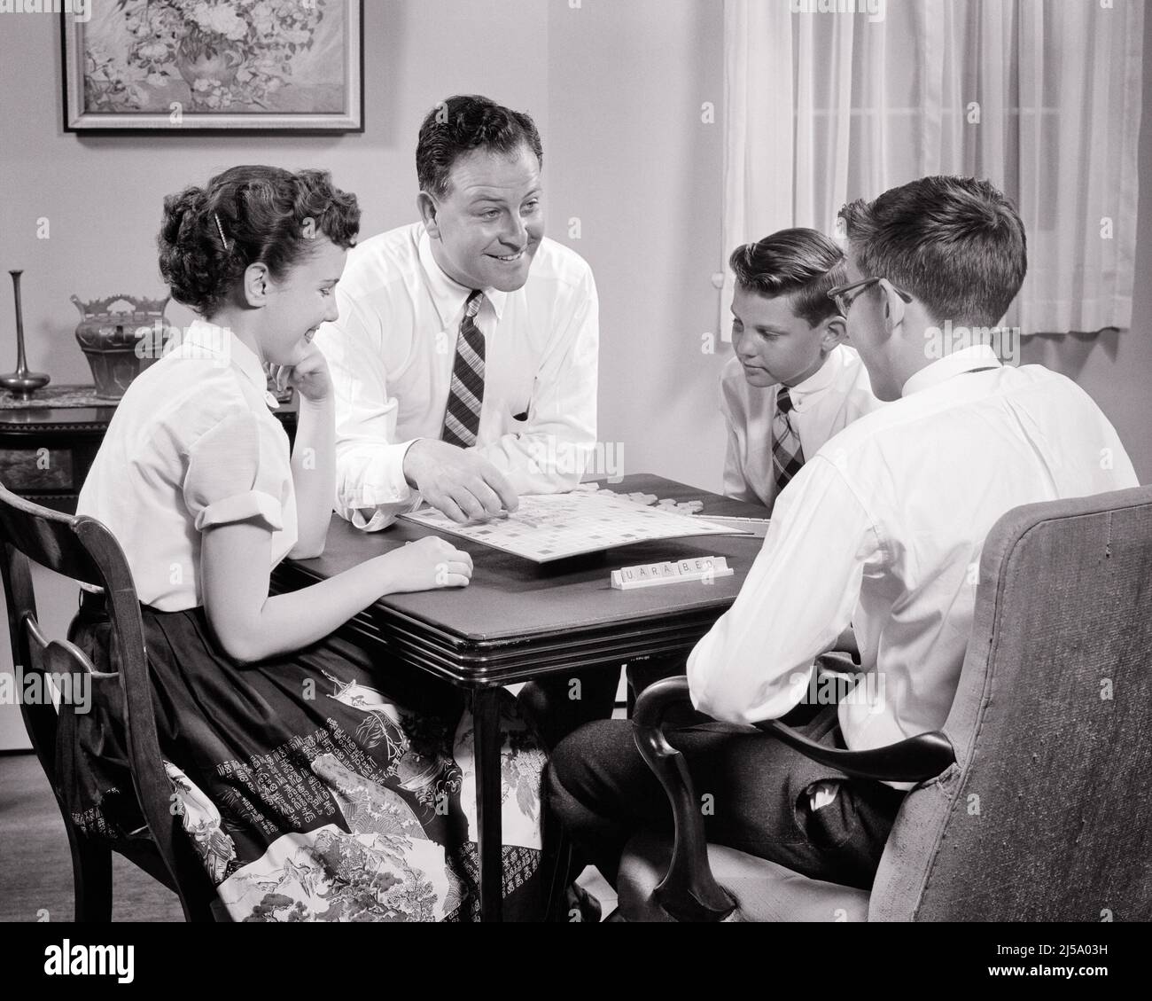 1950s FATHER PLAYING GAME OF SCRABBLE WITH HIS THREE TEENAGE KIDS A GIRL AND TWO BOYS SITTING AT LIVING ROOM FOLDING CARD TABLE - j7355 HAR001 HARS PAIR 4 SUBURBAN URBAN OLD TIME NOSTALGIA BROTHER OLD FASHION SISTER 1 JUVENILE COMMUNICATION SPELLING COMPETITION INFORMATION SONS FAMILIES LIFESTYLE CELEBRATION FEMALES BROTHERS HOME LIFE HALF-LENGTH DAUGHTERS PERSONS CARING MALES TEENAGE GIRL TEENAGE BOY ENTERTAINMENT FOLDING SIBLINGS CONFIDENCE SISTERS FATHERS B&W ACTIVITY HAPPINESS HIS STRATEGY LIVING ROOM AND WORD CHOICE DADS EXCITEMENT KNOWLEDGE RECREATION PRIDE CARD TABLE A AT OF OPPORTUNITY Stock Photo