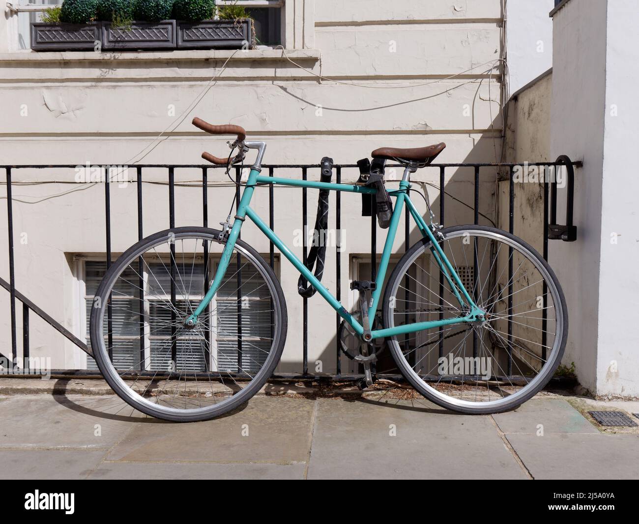 London, Greater London, England, April 09 2022: Pale blue cycle with brown seat and handle bars chained to railings of a house. Stock Photo