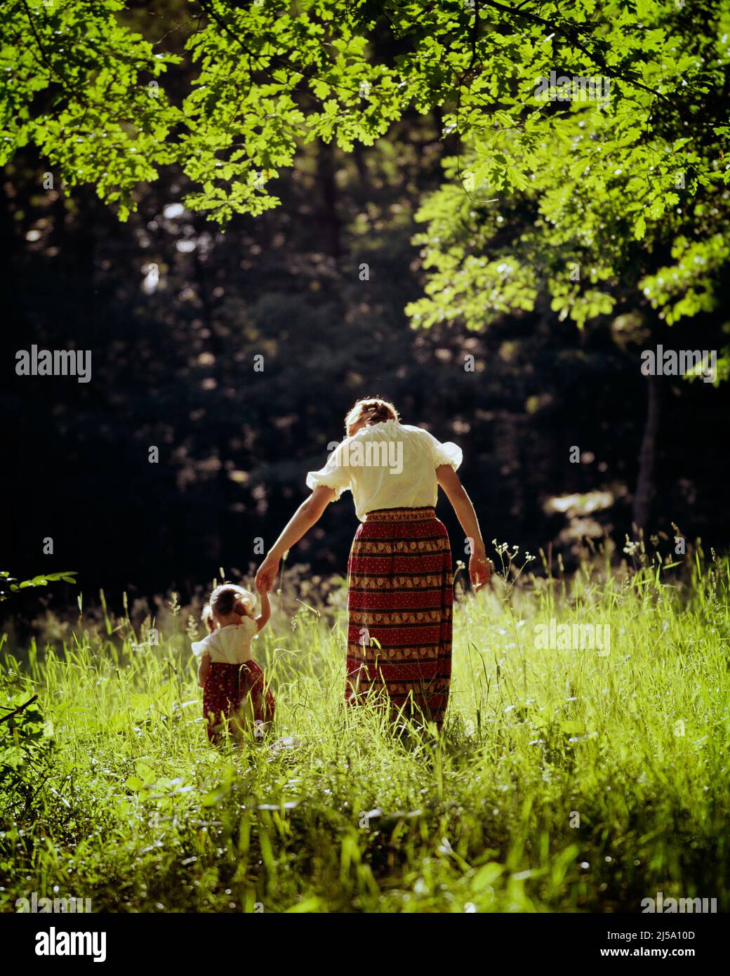 1970s REAR VIEW OF WOMAN MOTHER AND CHILD DAUGHTER WALKING IN SUNLIT