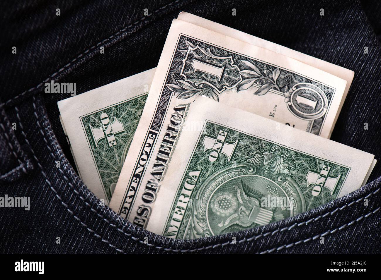 Three dollar bills stick out in the pocket of black jeans. Saving